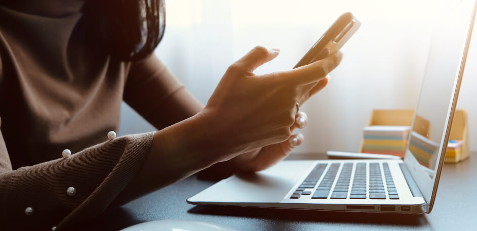 Woman in front of laptop looking in mobile